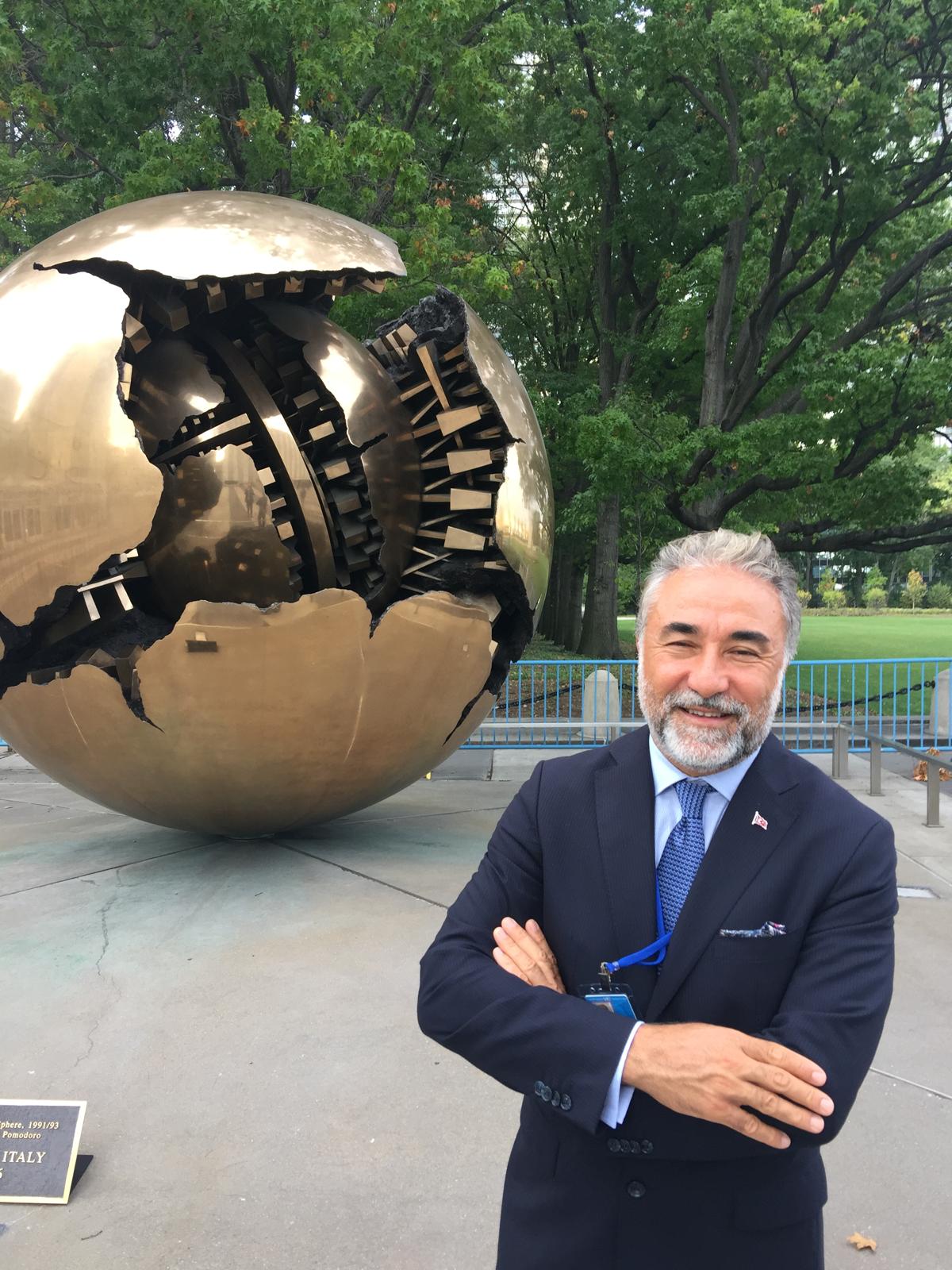 Cahit Şahin at an outdoor event, standing in front of a globe sculpture